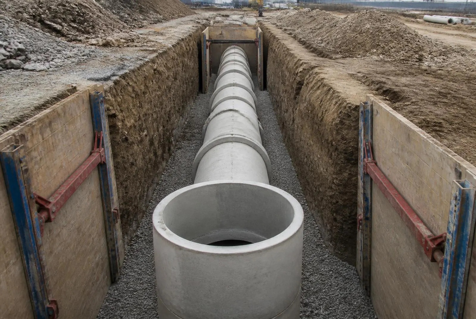 Verbauter Rohrgraben mit Betonrohrleitung auf Kiesbettung und gesetztem Schachtring